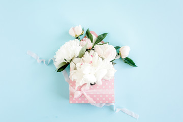 White bouquet of peonies in an envelope for flowers on blue background. Minimal floral concept greeting card. Flat lay, top view. 