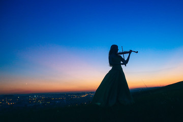 Girl in an evening dress plays the violin, sunset, silhouette