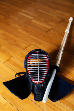 High angle close up of Kendo mask and wood sword on hardwood floor.