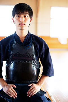 Male Japanese Kendo fighter kneeling on floor, looking at camera.