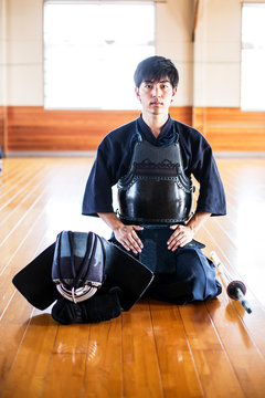 Male Japanese Kendo fighter kneeling on wooden floor, looking at camera.