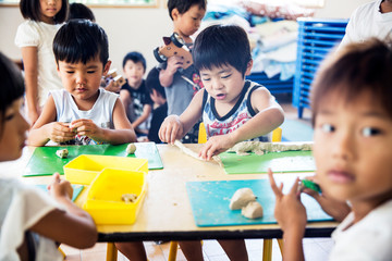 Group of children sitting at table in a Japanese preschool, doing crafts..
