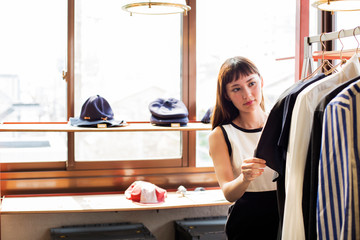 Japanese saleswoman standing in clothing store, looking at shirt.