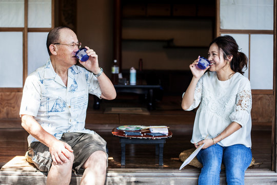 Japanese man and woman sitting on floor on porch of traditional Japanese house, drinking tea.
