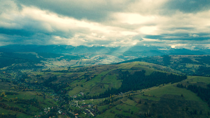 Fototapeta na wymiar Aerial drone view of beautiful mountain valley with green pine trees and hills. Scenic landscape. Gloomy day. Sun rays trough the clouds