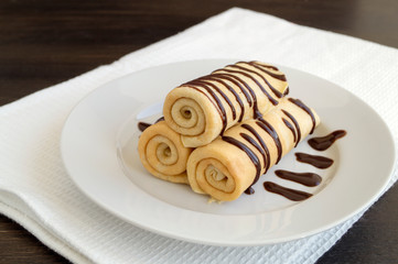 Homemade pancakes twisted with chocolate on a white plate.