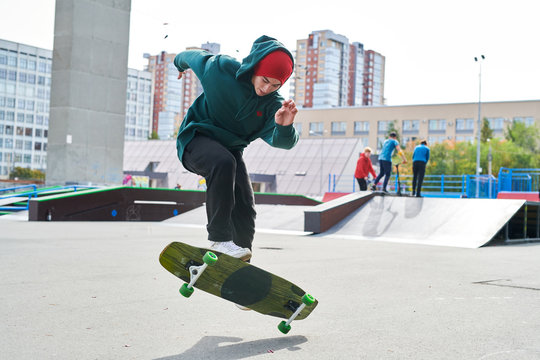 Full length portrait of modern teenager doing longboard stunts in extreme park, copy space