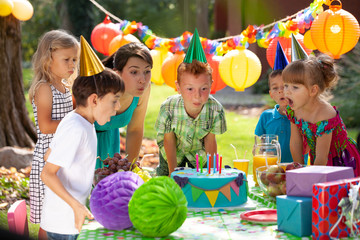 Kids blowing out candles on birthday cake during colorful party in the garden