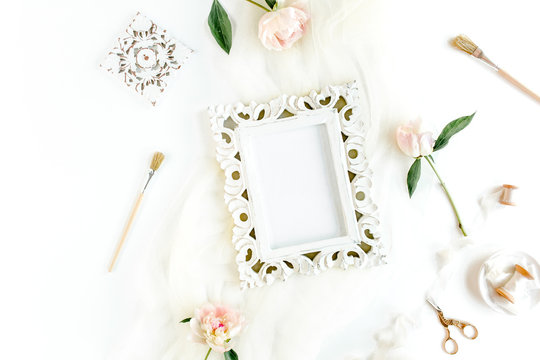 Carved, white frame decorated of white peony flowers, accessories on white background. Flat lay, top view.