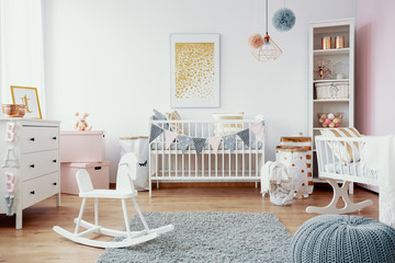 Bright baby room with white furniture, grey carpet on the floor and golden painting on the empty...