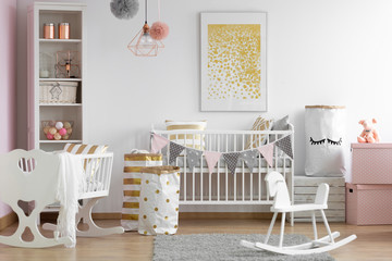 White wooden rocking horse, crib and nursery in stylish scandinavian baby room interior with white and gold accents, real photo