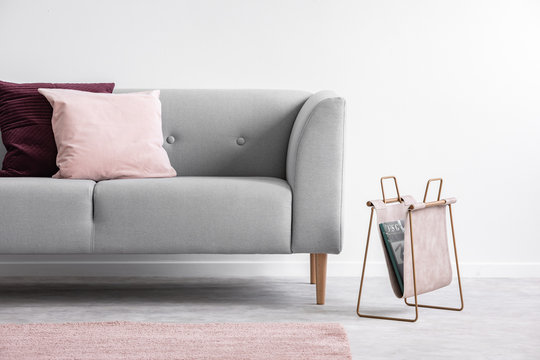 Organizer with newspaper next to grey couch with cushions in loft interior with pink rug. Real photo