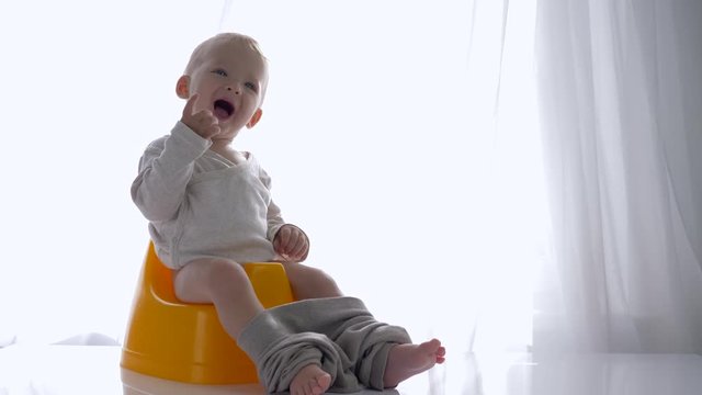 emotion joy of healthy toddler boy sitting and laughs on potty in bright room close-up