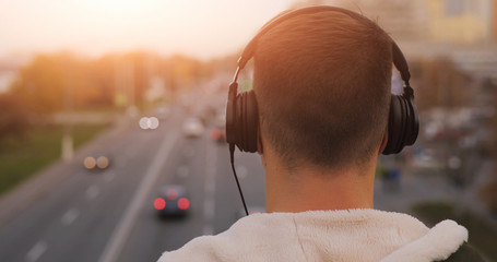 Back view of man listening to music with headphones in city
