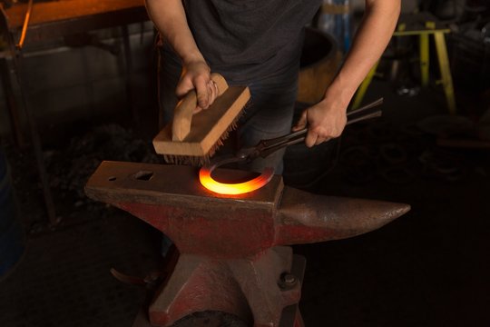 Female metalsmith brushing horseshoe in factory