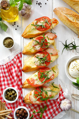Bruschetta, grilled slices of baguette with mozzarella cheese, tomatoes, garlic and aromatic basil on a white wooden table, top view. A delicious Mediterranean appetizer