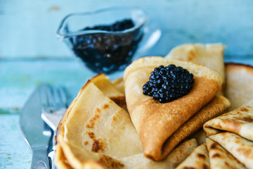 Pancakes with black caviar and sour cream on a wood table in a white plate