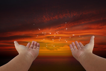 Human hands pray with sunset background.