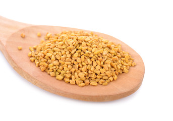 dry fenugreek seeds in wooden spoon on white background