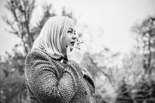 A pretty big European girl with overweight smokes in an outdoor . Problems of smoking among women. The effect of smoking on weight and shape 