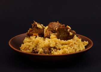 clay plate with rice pilaf, meat, turmeric on black background