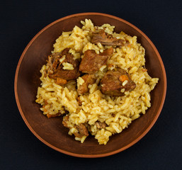 clay plate with rice pilaf, meat, turmeric on black background