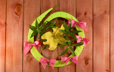 Fototapeta na wymiar English green letter O made of plywood with a bow and a bud of a yellow lily, laid out on a wooden background