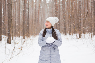 Winter, season and people concept - Woman in grey coat and white hat walking in winter park and playing with snow