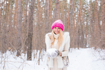 Fototapeta premium Season and people concept - Attractive blond woman dressed in white coat and pink hat standing in winter snowy park