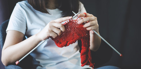 Close up shot of young woman hands knitting a red scarf handicraft in the living room on terrace at...