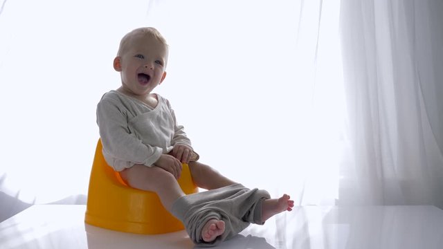 little emotional child boy sitting on chamberpot and laughs in bright room close-up