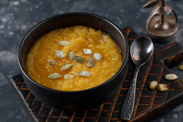 Pumpkin cream soup in bowl on black concrete background. Closeup view, selective focus.