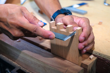 Skilled joiner working in carpentry. Amateur woodworker making dovetail join for wooden drawer in...
