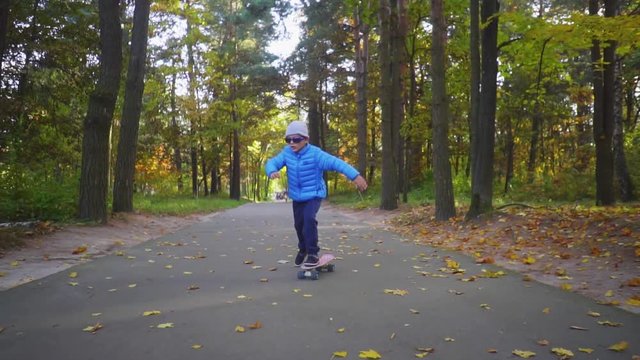 Child on skateboard boy ride on skate outdoor in autumn park
