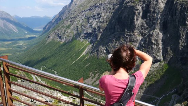 Tourist woman with camera taking picture from Trollstigen Trolls Path winding scenic mountain road in Norway Europe. National route. Travel destination