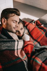 Fototapeta premium high angle view of happy young couple relaxing on couch and covering with plaid