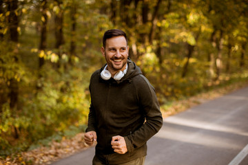 Young man running in the autumn forest with earphones