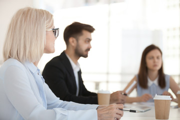 Obraz premium Diverse employees sit at table having discussion at business meeting in office, colleagues negotiate in boardroom, workers talking at briefing, businesspeople discuss project in conference room