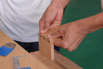 Skilled joiner working in carpentry. Amateur woodworker making dovetail join for wooden drawer in carpenters workshop
