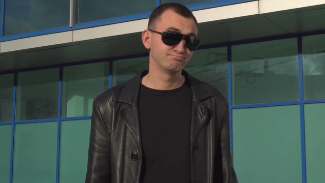 Young serious man in leather jacket and sunglasses does not accept offer by shaking head outdoor