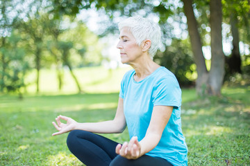 Senior woman in a lotus position   on a grass