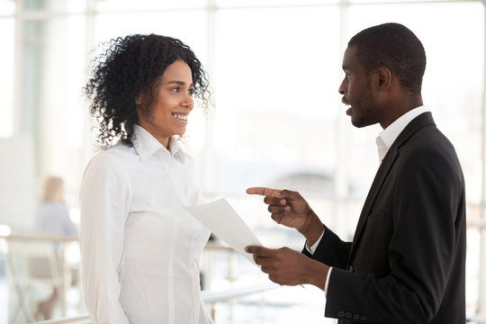 African American businessman talk to excited female black employee, telling good news about promotion or achievement, boss praise intern, diverse millennial workers chat in hallway. Reward concept