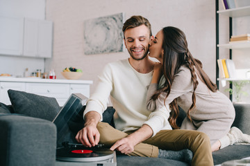 happy young couple listening music with vinyl record player and cuddling at home