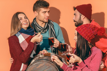 Smiling european men and women during party photoshoot. The guys posing as friends at studio fest with wineglasses with hot mulled wine on foreground.