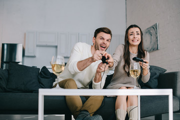 expressive young couple playing retro video game on couch at home