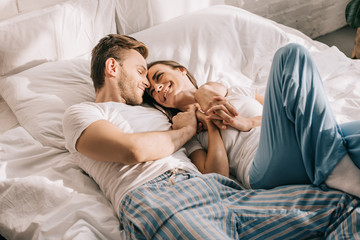 beautiful young couple in pajamas cuddling in bed in morning