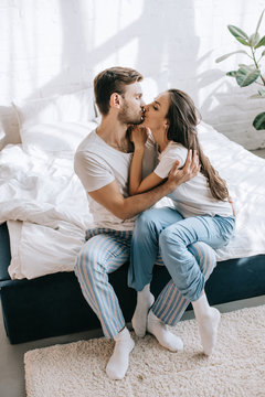 beautiful young couple in pajamas kissing while sitting on bed in morning  Stock Photo | Adobe Stock
