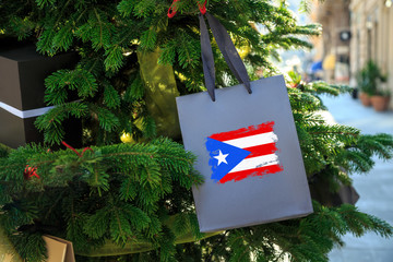 Puerto Rico flag printed on a Christmas shopping bag. Close up of a shopping bag as a decoration on a Xmas tree on a street. New Year or Christmas shopping, local market sale and deals concept.  - 231929191