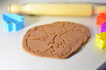 Christmas ginger baking on wooden table with blurred colorful new year tree forms for holiday pastries on background and wooden rolling pin