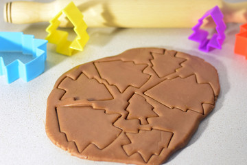 Christmas ginger chocolate dough for holiday cookies with cutting new year trees and colorful blurred forms on background and wooden rolling pin